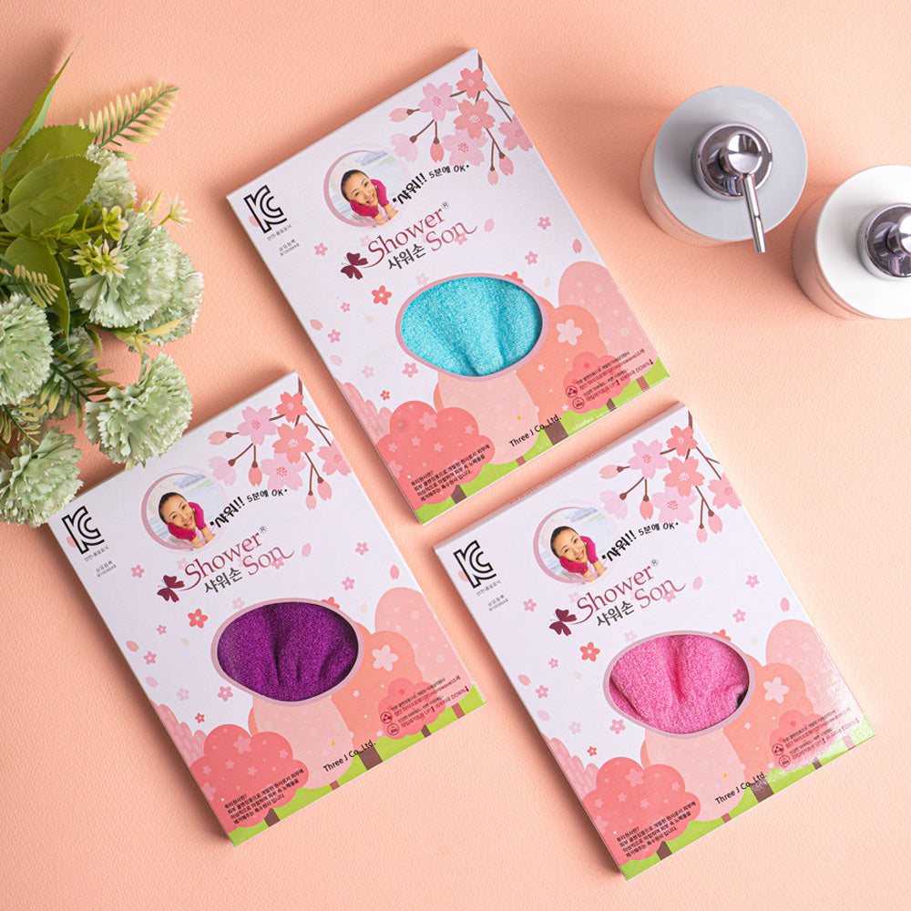 Three boxes of Korean exfoliating viscose shower gloves in aqua, pink, and purple on peach background